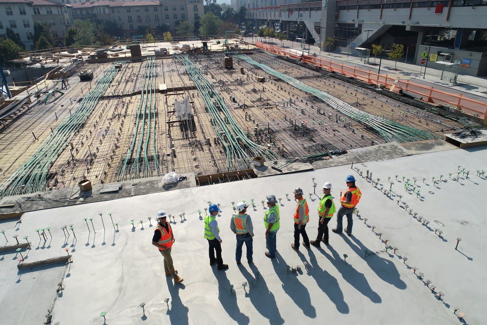 A survey crew walks across a large graded construction site with rebar laid out in rows